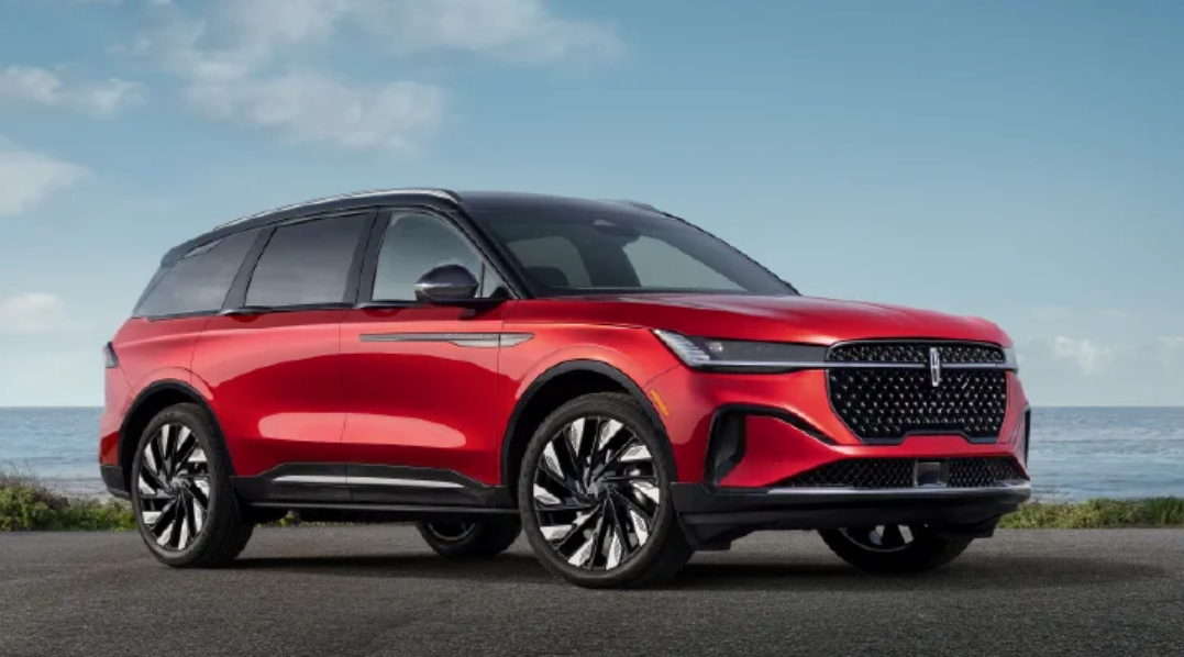 Red 2026 Lincoln Nautilus SUV parked on a coastal road in Houston, TX, featuring a sleek design, large alloy wheels, and a bold front grille with ocean backdrop.