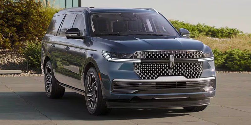 Gray 2026 Lincoln Navigator SUV parked on a paved driveway in Houston, TX, showcasing a bold chrome grille, LED headlights, and a spacious luxury design with landscaped greenery in the background.