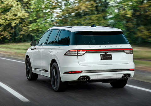 A white 2025 Lincoln Aviator® SUV is being driven away down a road lined with colorful trees. | Bayway Lincoln in Houston TX