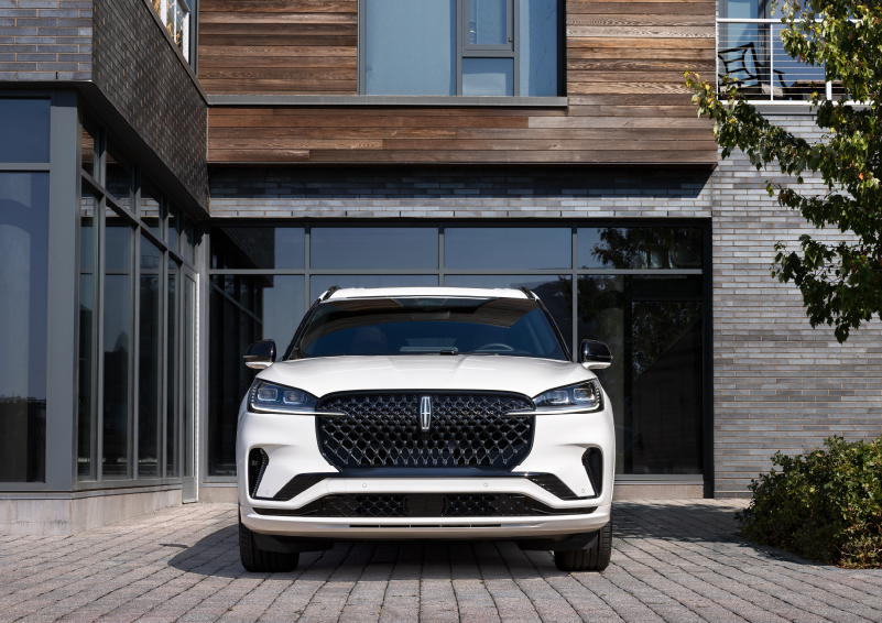 A white 2025 Lincoln Aviator® SUV is shown parked outside a modern building with gray brick and wood accents. | Bayway Lincoln in Houston TX