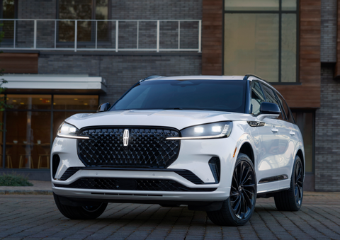 A white 2025 Lincoln Aviator® SUV is shown parked outside a modern building with gray brick and wood accents. | Bayway Lincoln in Houston TX