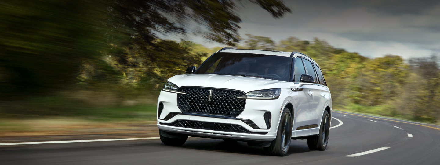 A white 2025 Lincoln Aviator® SUV is being driven down a road lined with trees. | Bayway Lincoln in Houston TX