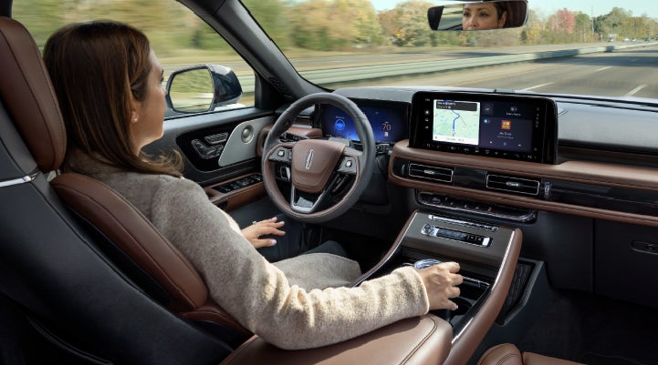 A 2027 Lincoln Aviator® SUV is being driven hands-free on a highway lined with trees. | Bayway Lincoln in Houston TX