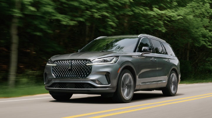 A 2027 Lincoln Aviator® SUV is being driven down a road lined with trees. | Bayway Lincoln in Houston TX